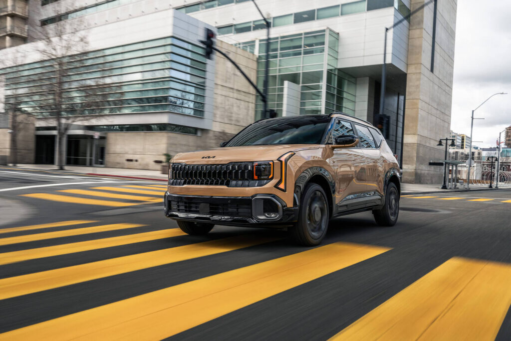 2027 Kia Seltos X-Line in bronze crossing a yellow-striped city intersection