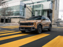 2027 Kia Seltos X-Line in bronze crossing a yellow-striped city intersection
