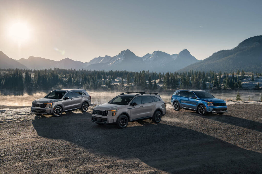Three 2027 Kia Sorentos parked beside a mountain lake at sunrise