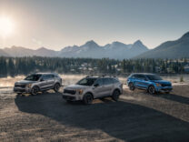 Three 2027 Kia Sorentos parked beside a mountain lake at sunrise