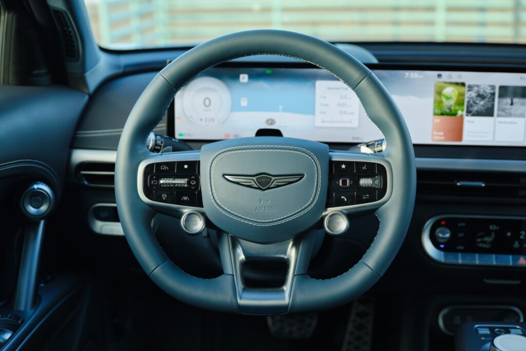 Steering wheel of a 2026 Genesis GV60 with its drive mode and boost buttons